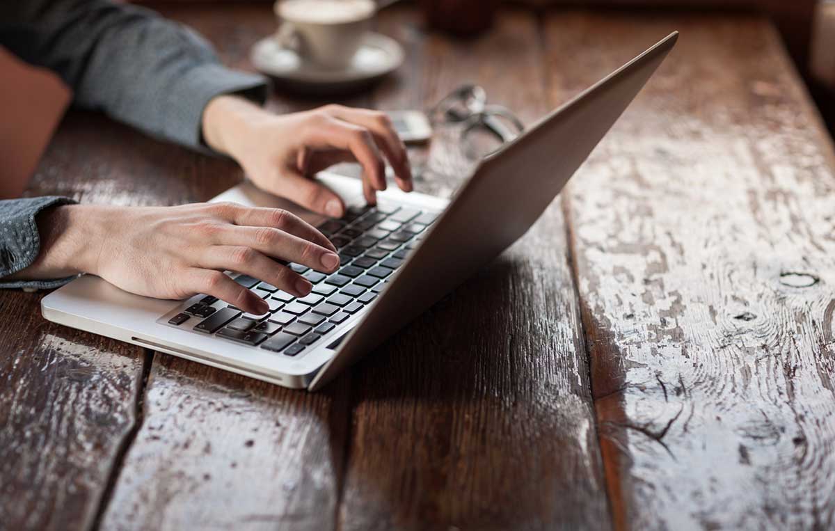 Close up picture of a man's hands typing on a laptop.