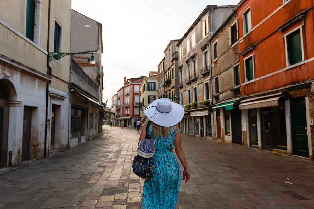Woman wearing blue dress and white hat walking in street in Venice, Italy