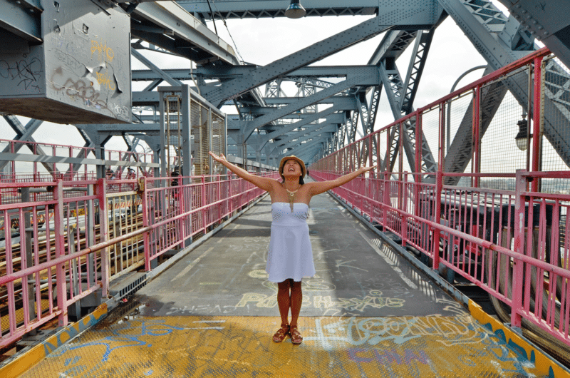 woman walking the Williamsburg Bridge Pedestrian Path and posing under steel beams