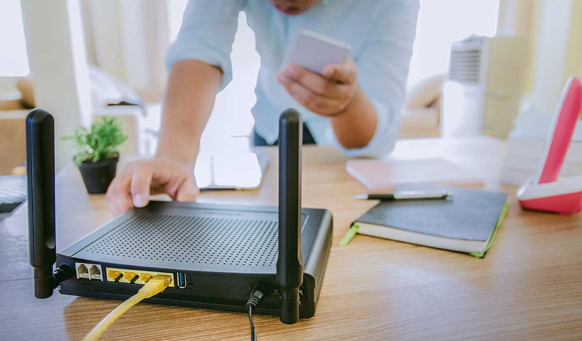 Closeup of a wireless router and a man using smartphone on living room at home office.