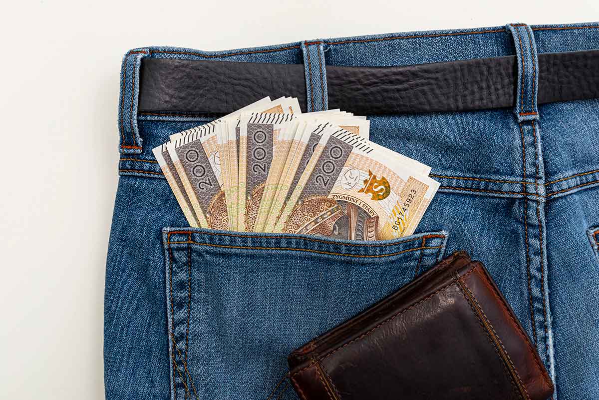 A lot of Polish banknotes with a nominal value of 200 PLN inserted into the back pocket of blue denim pants. Visible brown leather wallet.