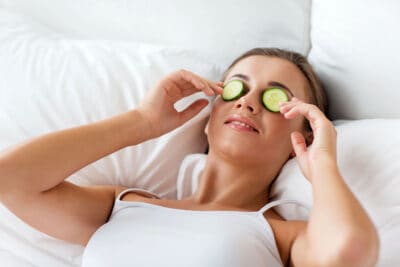 Woman applying cucumbers to face at home.