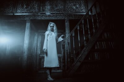 ghost-like figure walking down the stairs of a haunted hotel