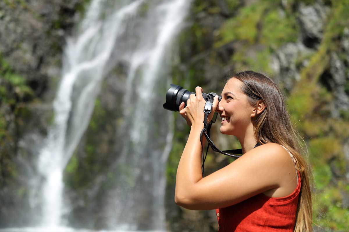 Side view portrait of a happy woman taking photos with mirrorless camera in nature.