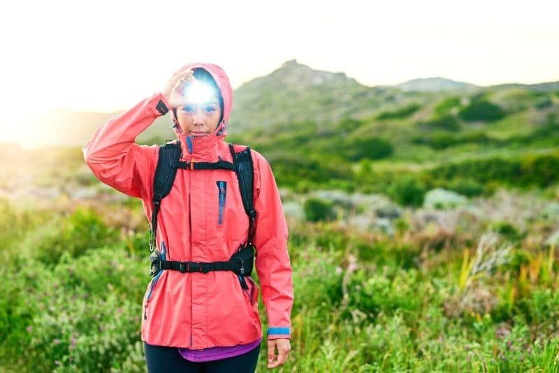 woman hiking solo while wearing a solo hiking essentials like a headlamp and rain coat