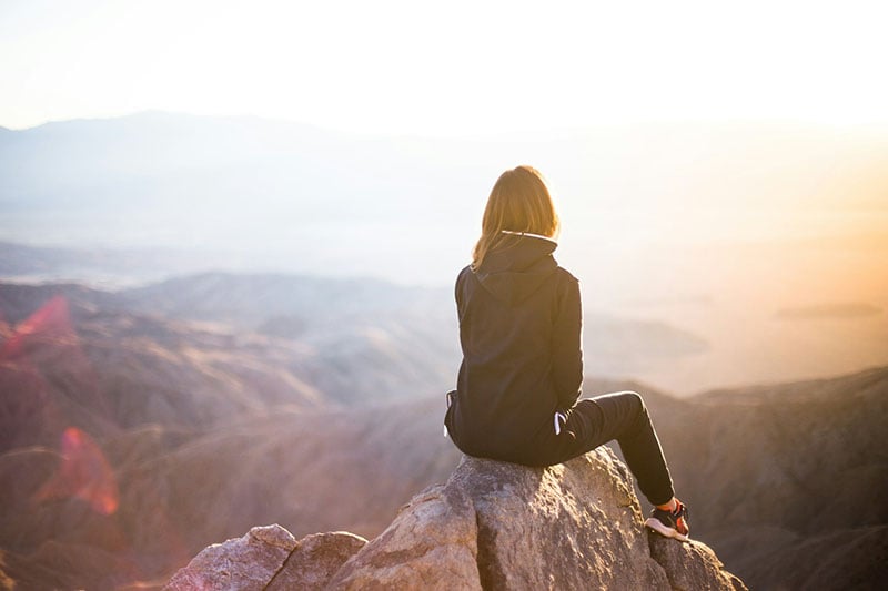 A woman contemplating a mountain view at sunset.