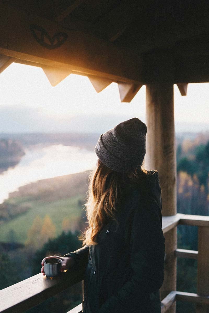 A woman holding a cup of coffee in her hand and admiring the views of a lake.