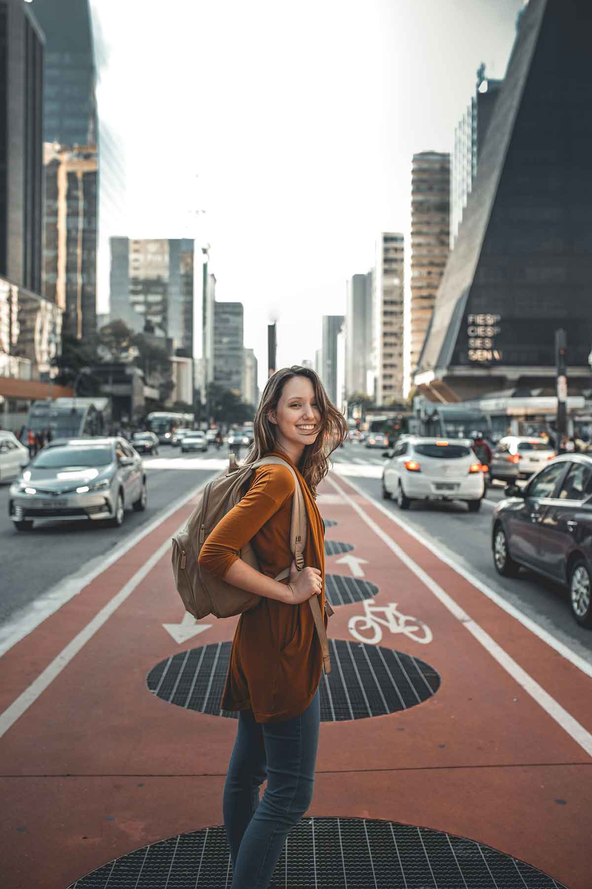 A woman with a backpack crossing a road in a big city.