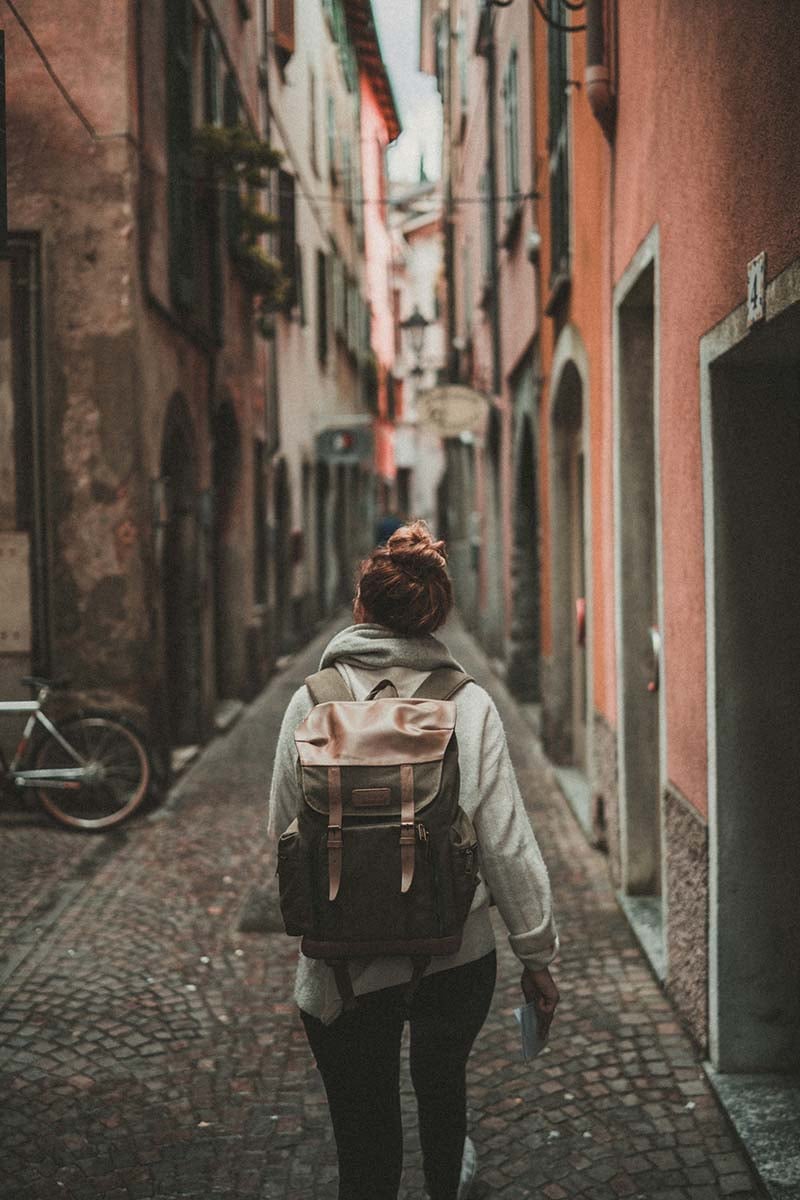 A woman with a backpack walking down a narrow street in Varenna, Italy.