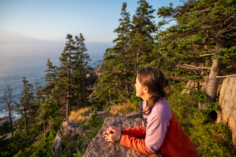 woman watching the sunrise in Acadia National Park after hiking to Otter Cliff