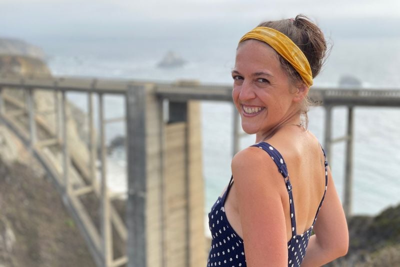 woman smiling with the Bixby Bridge in the background on a solo US road trip