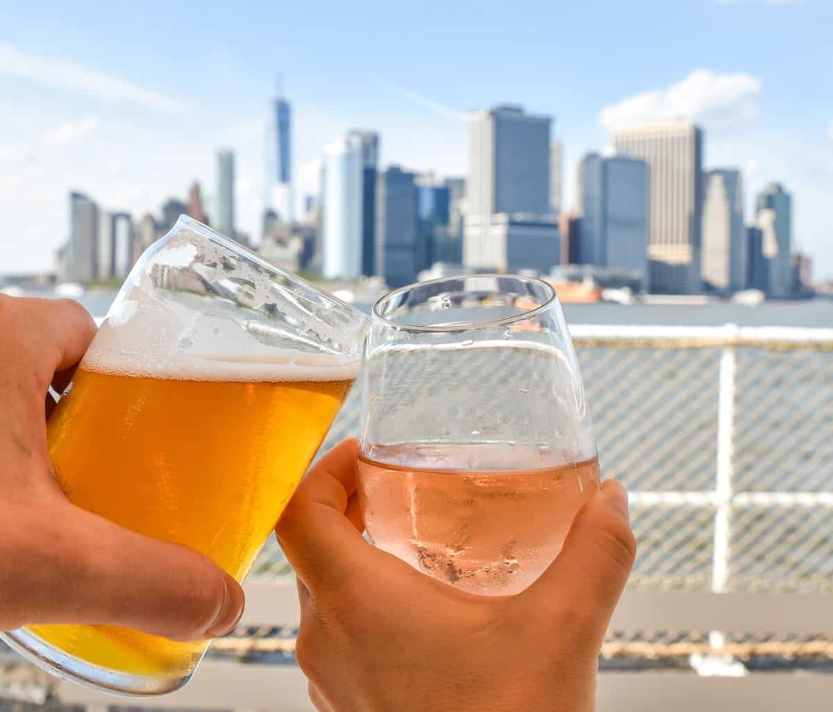 couple clicking drink glasss on Governors Island while looking out toward the Manhattan skyline