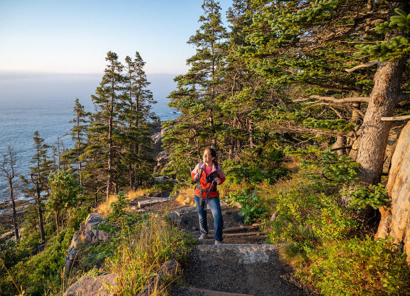 woman hiking the Ocean Path Trail at sunrise in Acadia National Park