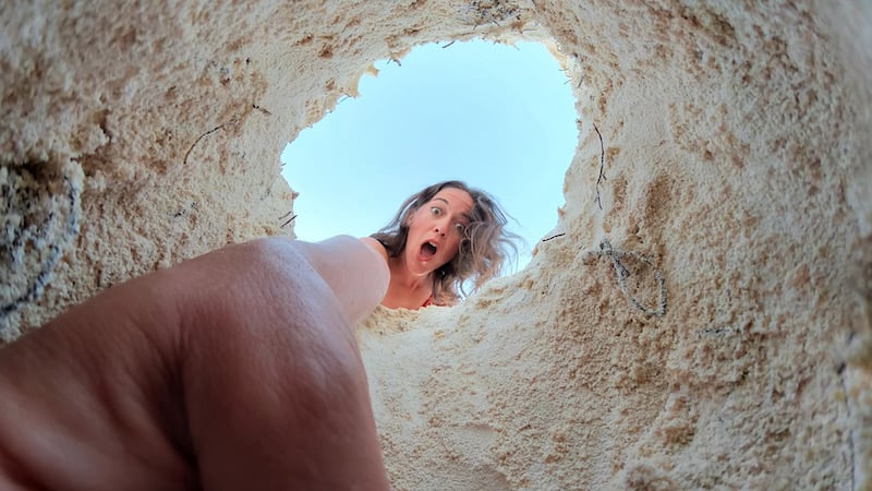 female travel blogger digging in sand on the beach 