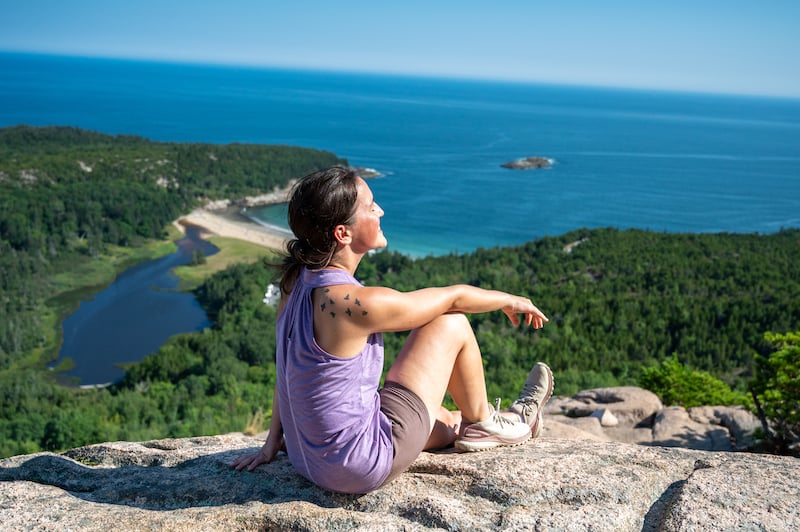 woman taking in the view from the Beehive Summit in Acadia National Park on a Maine road trip