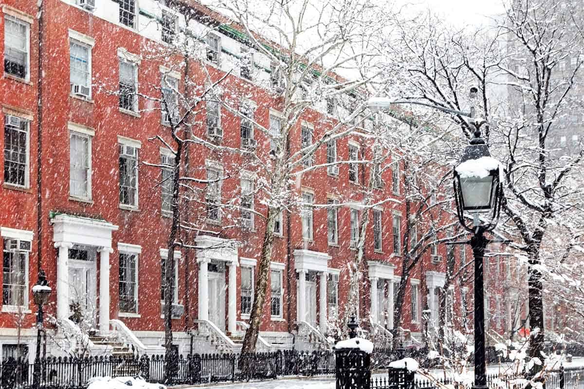 Snow covered winter street scene with old buildings along Washington Square Park.