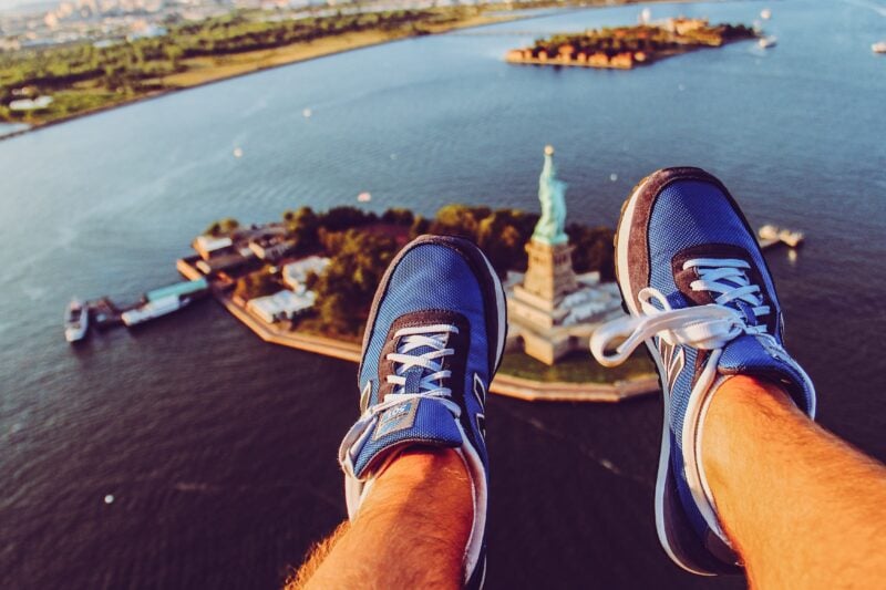 feet dangling out of a helicopter architectural tour of New York City with a view of the Statue of Liberty below