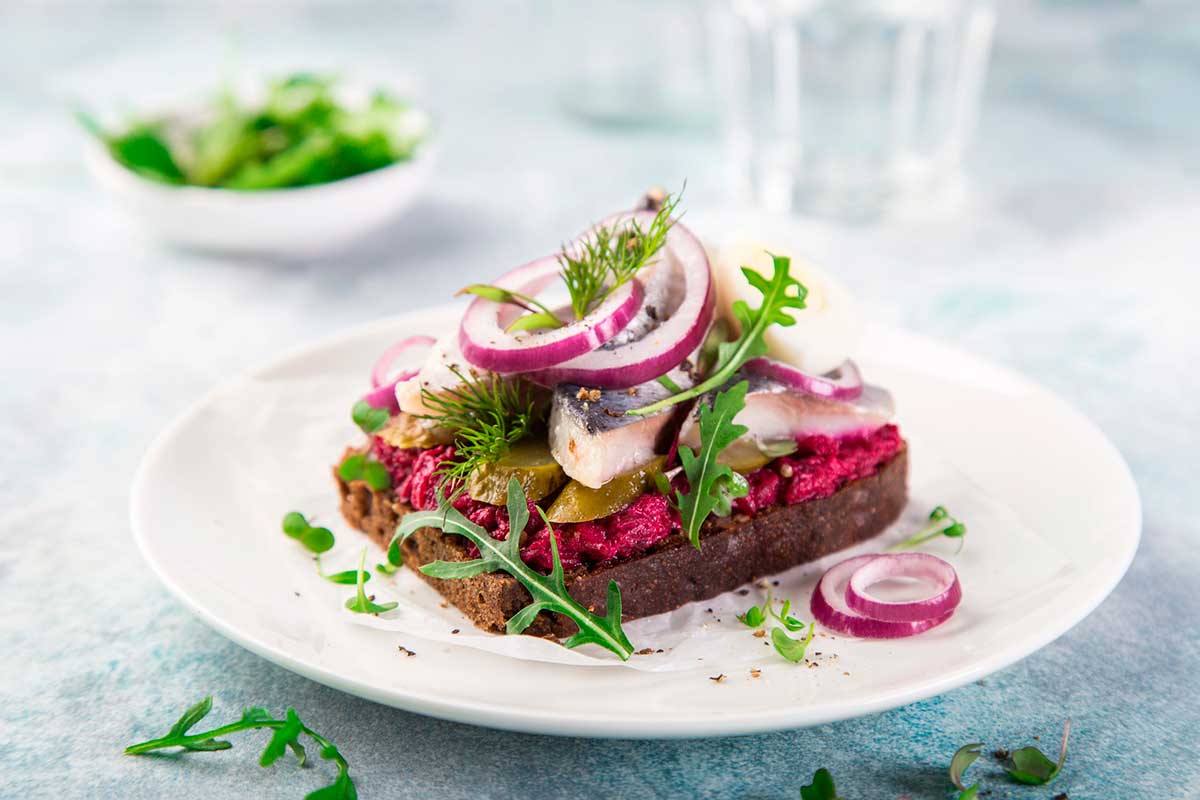 Open sandwich with dark rye bread, beet, marinated herring, pickled cucumber and red onion, smorrebrod.
