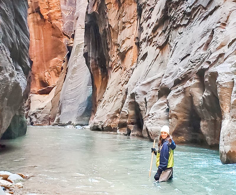 woman doing the best hikes in Utah and trekking through a stream in a deep canyon