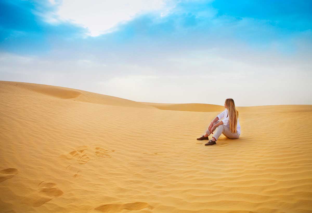solo female traveler in Morocco sat in the sand dunes of the Sahara Desert