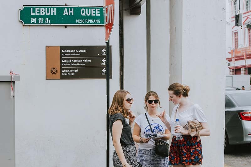 Three women standing beside a white wall in a street in Malaysia.