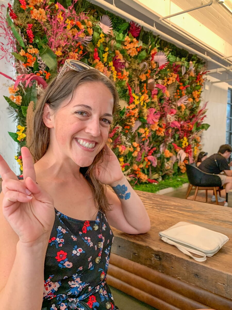woman posing for an Instagram photo in front of a colorful flower wall inside Industry City NYC