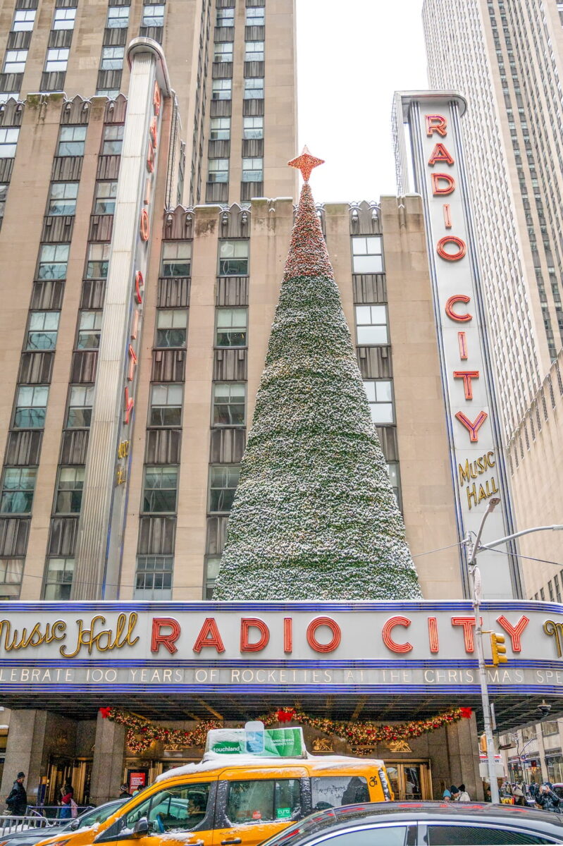 Radio City Music Hall marquee in NYC with a Christmas tree on top covered in snow