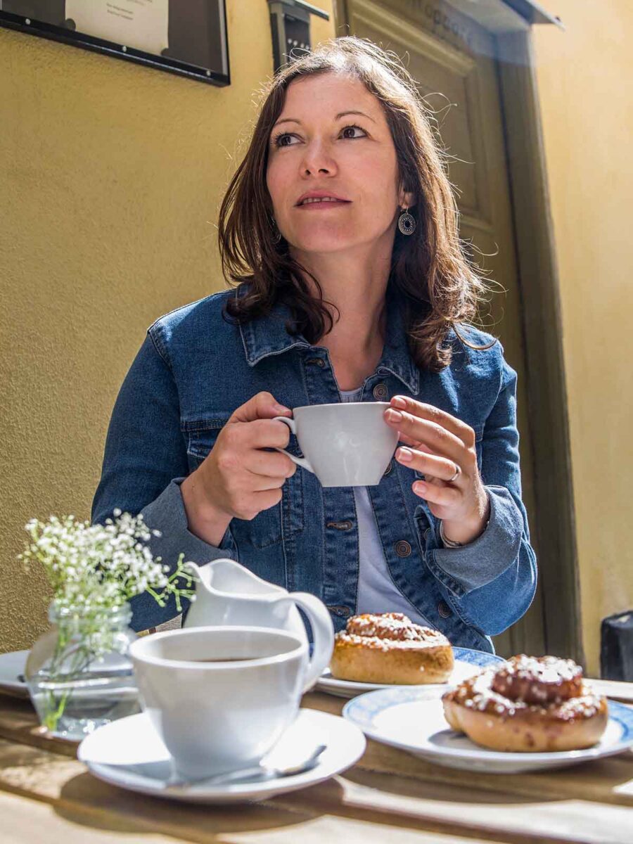 A woman enjoying Kanelbulle pastry and coffee at outdoor cafe in Stockholm.