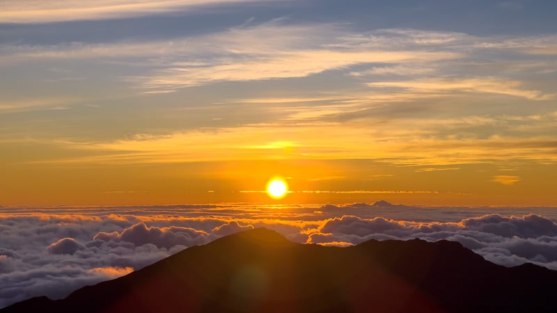 solo female traveler in Hawaii taking in a sunrise view from a volcano summit above the clouds in Maui