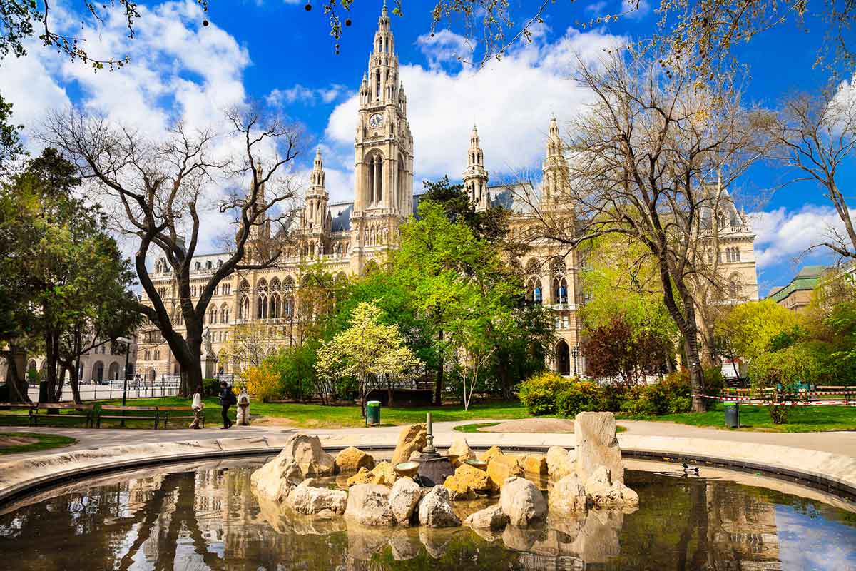 A beautiful park with a fountain and a building in the background.