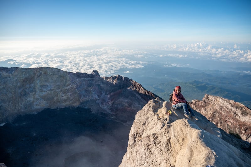 female traveler sitting on the crater rim of Mount Agung during a two week Bali itinerary