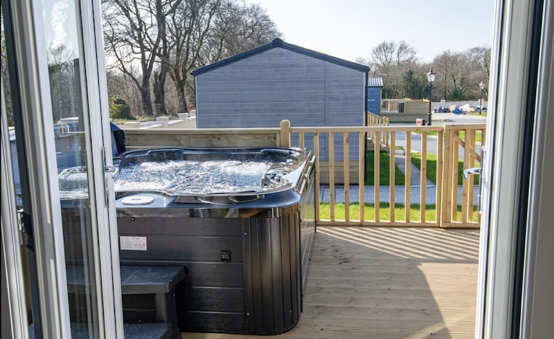sliding glass doors opening up to a wooden patio with an outdoor Jacuzzi at the Kilwinning Hot Tub Lodge in Glasgow, Scotland