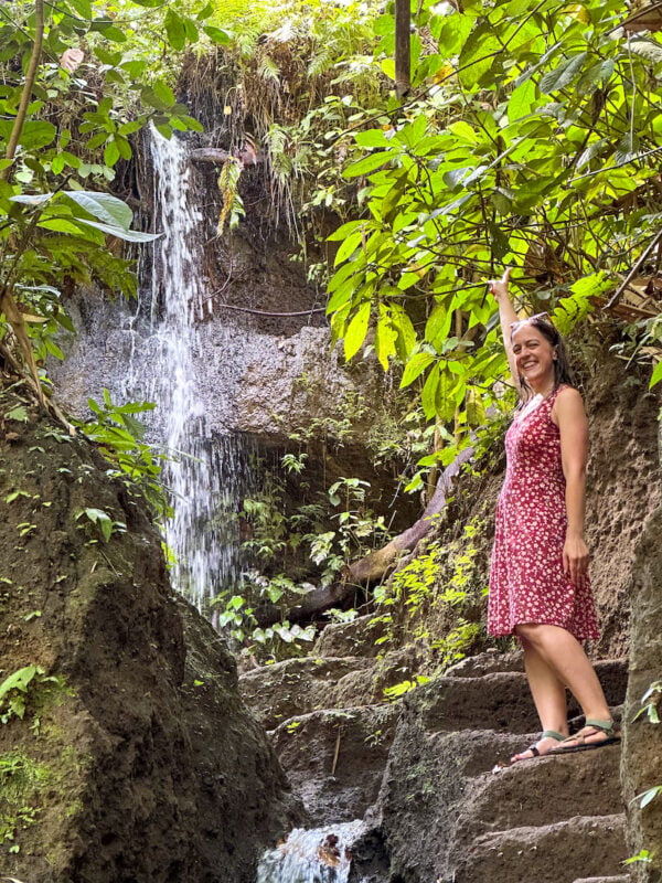 woman in a red dress posing in front of a small waterfall near Manuaba Waterfall