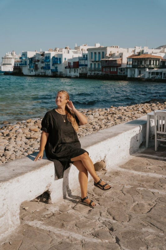 solo traveler in Greece posing in front of the white buildings of Little Venice in Old Town Mykonos 