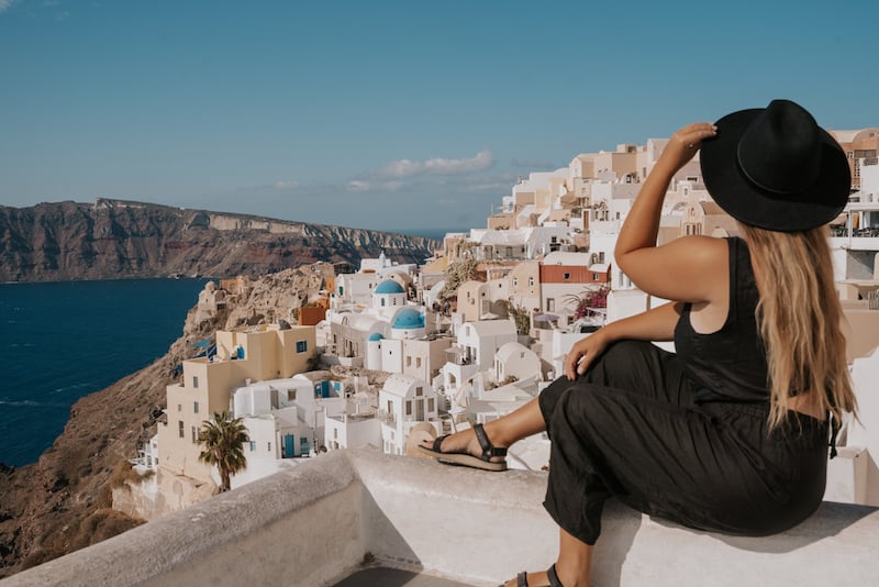 solo female traveler in Greece gazing out over the white and blue building of Santorini 