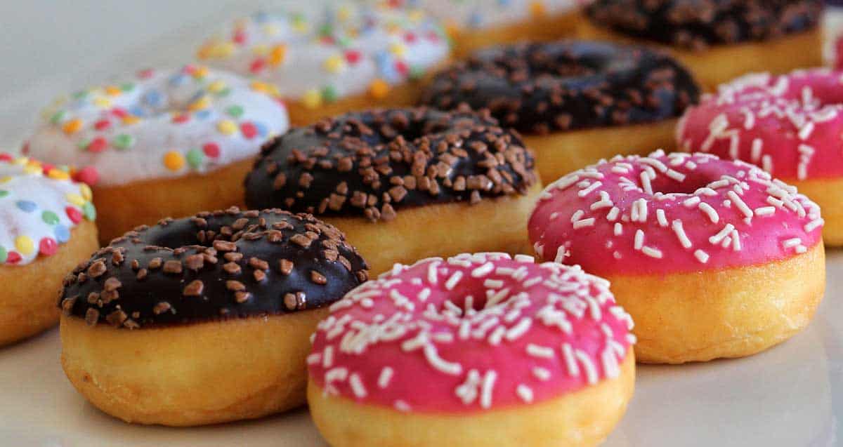 Close-up of colorful donuts on display during a NYC food tour, featuring pink, chocolate, and white frosted varieties topped with sprinkles and candy pieces.