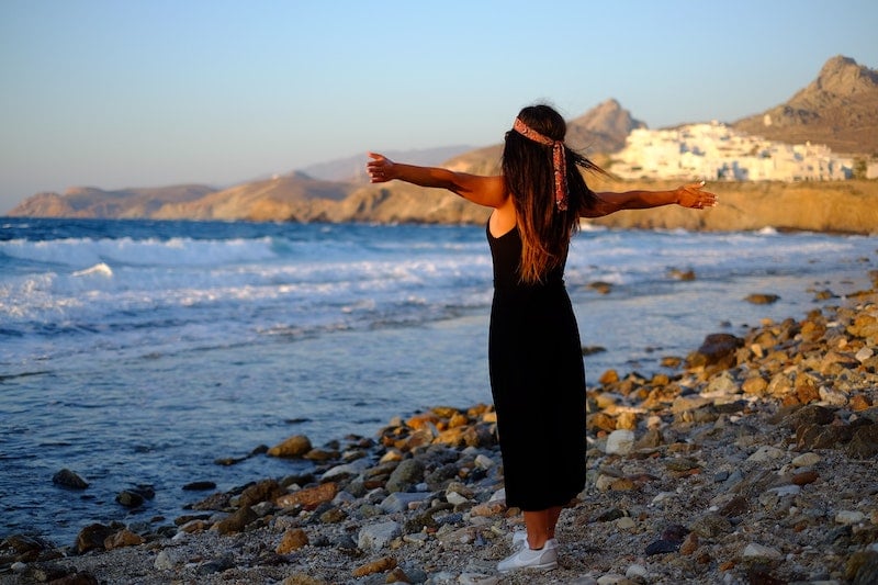 solo female traveler in Greece on a beach with outstretched arms 