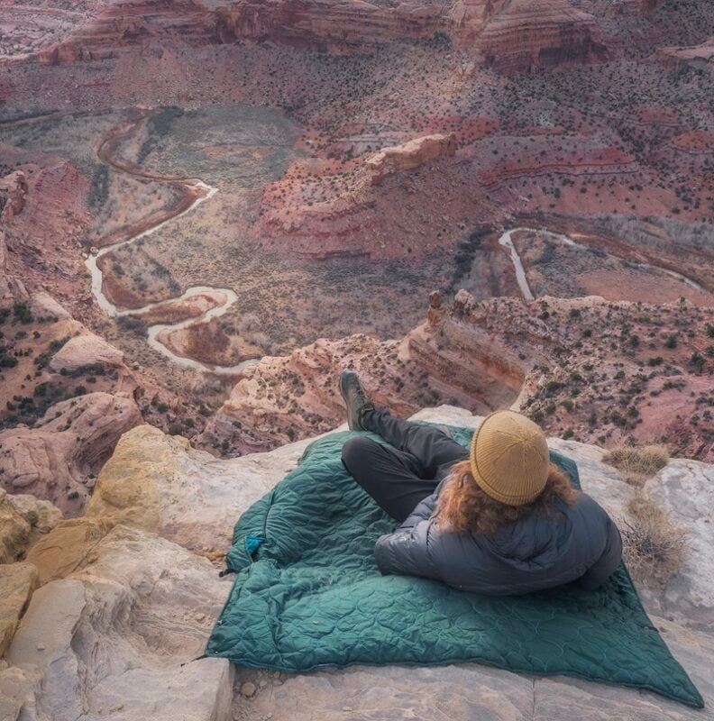 woman laying on a Coalatree hiking blanket on the top of a mountain