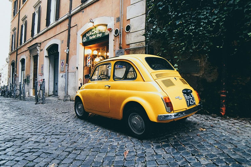 A yellow Fiat 500 car in a street in Rome, Italy.