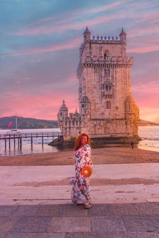 solo female traveler smiling in front of Belém Tower at sunset