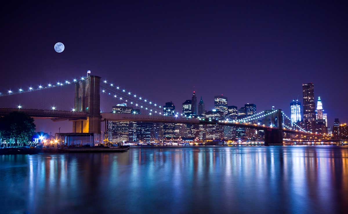 Traveler viewing the Brooklyn Bridge lit up over the East River on an NYC night tour.