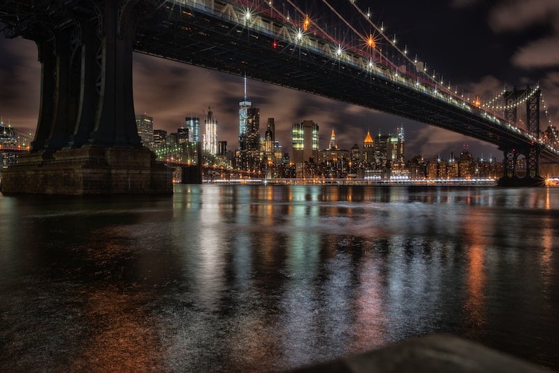 traveler viewing the Brooklyn Bridge lit up over the East River on an NYC night tour