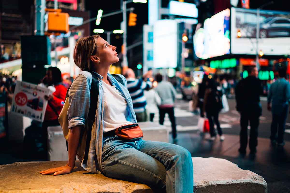 Young female traveler fascinated with Time square lights sitting on crowded street