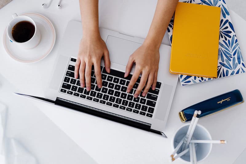 hands typing on a laptop with notebooks nearby