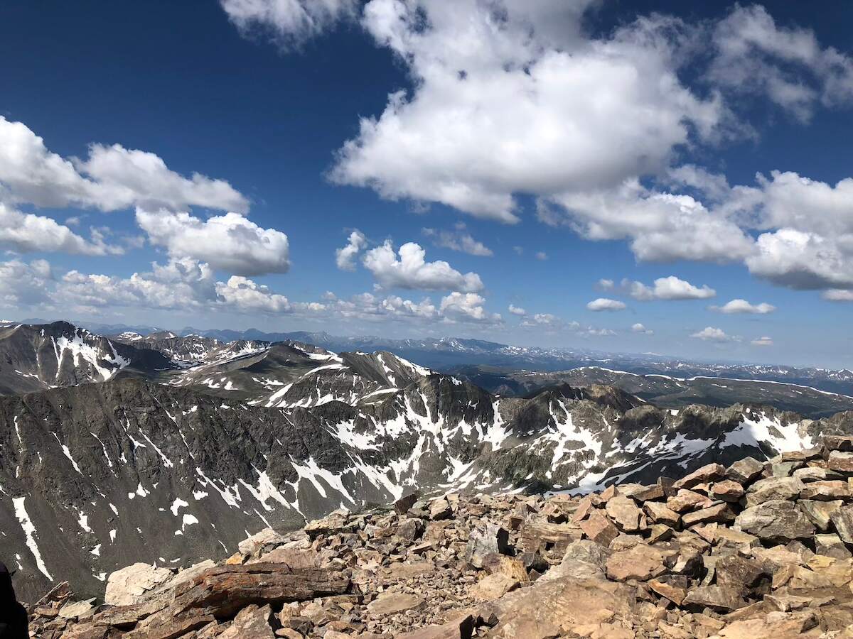 Stunning panoramic view of snow-capped mountains and rocky terrain under a partly cloudy blue sky, showcasing the hiking trails near Breckenridge. A perfect road trip destination from Denver, Colorado.