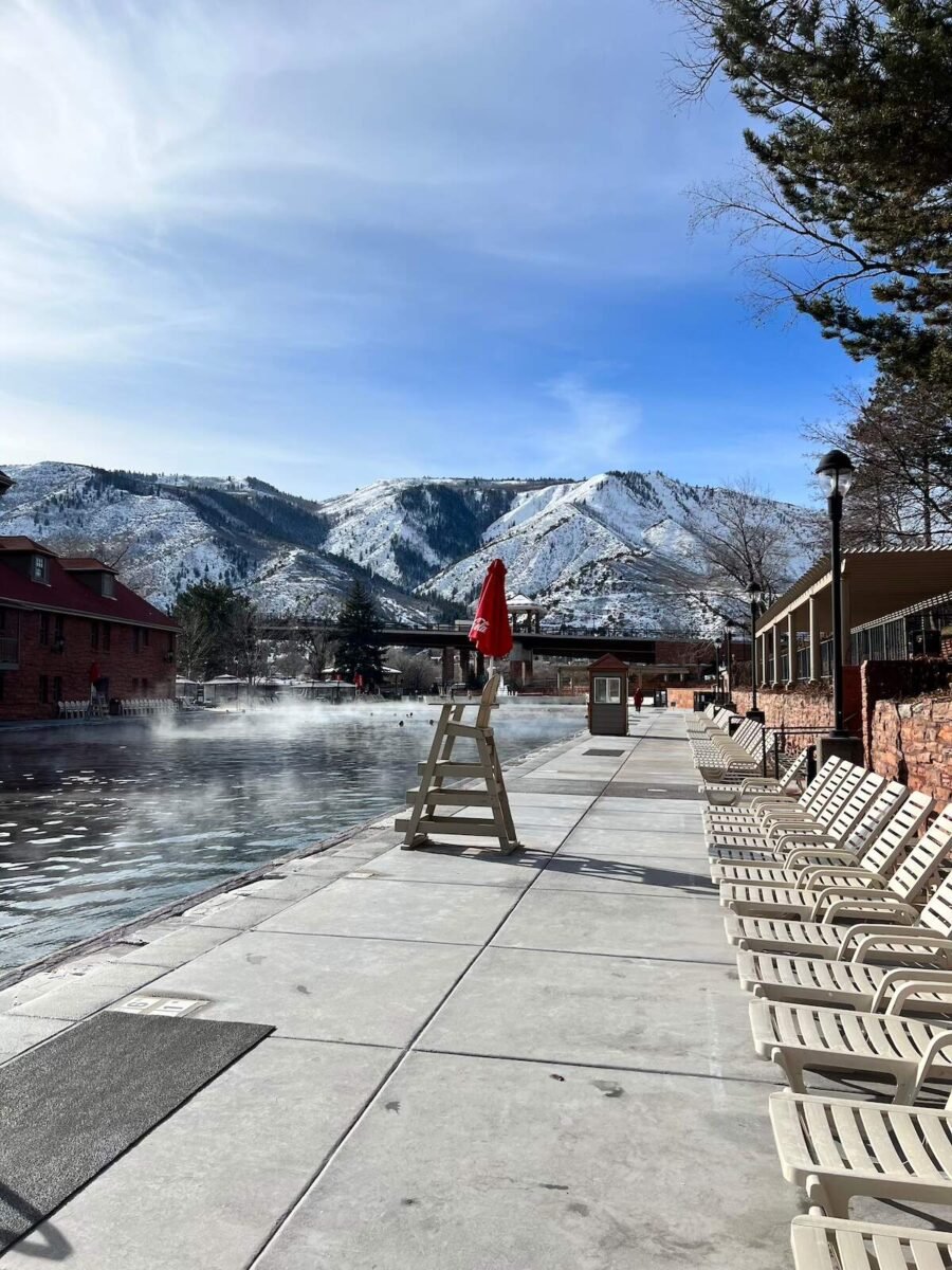 Outdoor hot springs pool at Glenwood Springs Hot Springs Resort, with steam rising from the water, surrounded by snow-covered mountains and buildings. A relaxing road trip destination from Denver, Colorado.