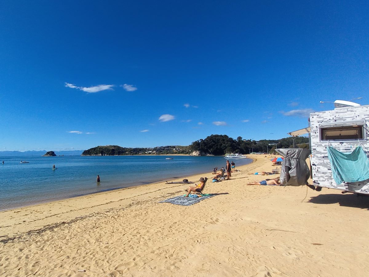 people relaxing on the golden sand of the beautiful Kaiteriteri Beach in New Zealand