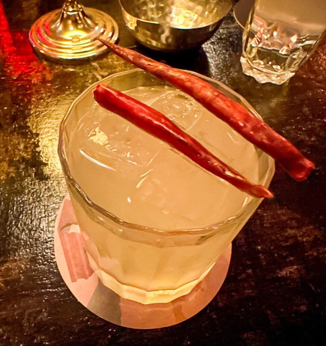 A spicy cocktail at Keys & Heels, a speakeasy in the Upper East Side of New York City, garnished with two red chili peppers and served over ice in a glass.