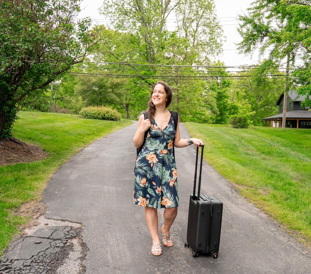 woman in a blue dress rolling a LEVEL8 aluminum cabin luggage set down a driveaway