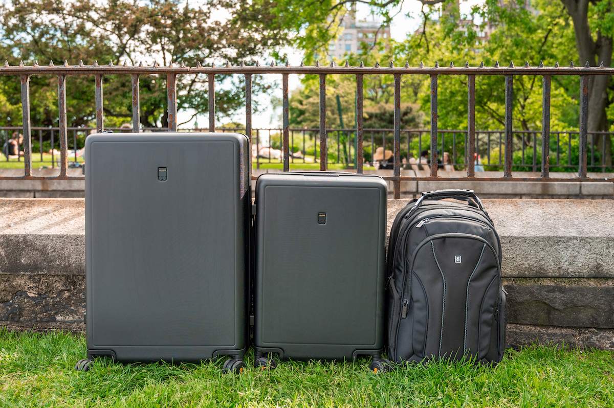 a row of three black LEVEL8 luggage pieces: an Atlas Laptop Backpack on top of a medium-sized Luminous Textured suitcase, with a larger suitcase to the left and a smaller carry on suitcase to the right